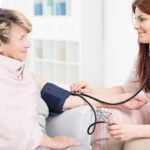 Young woman taking blood pressure of an elderly woman, sitting in light interior